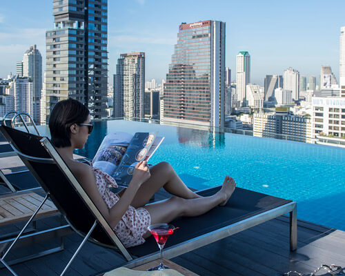 Hermosa chica leyendo una revista sentada en una silla comoda frente a la piscina del hotel Amara disfrutando sus vacaciones en bangkok