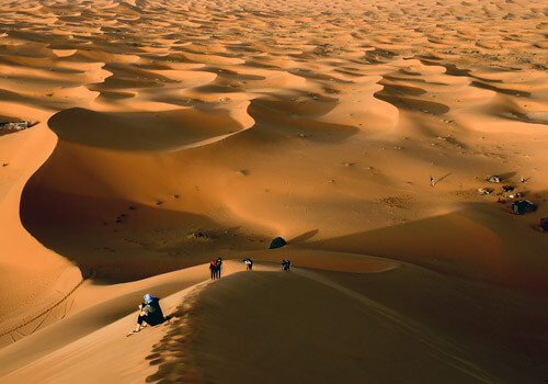 Imagen de viajeros caminando a traves del desierto bajo el cielo del sahara